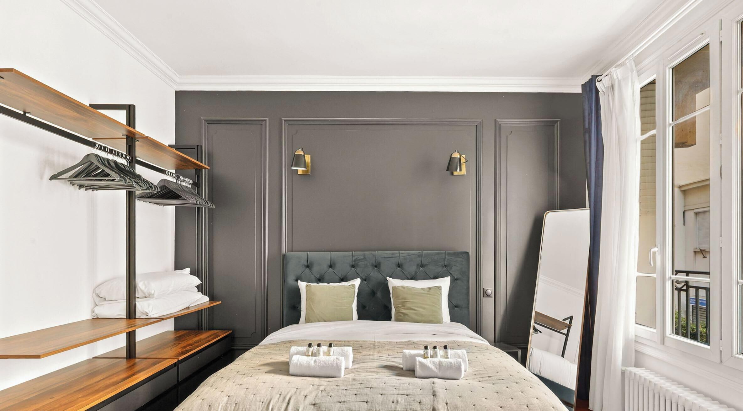 A hotel room with a bed, a wardrobe, a shelf with towels, and a window.