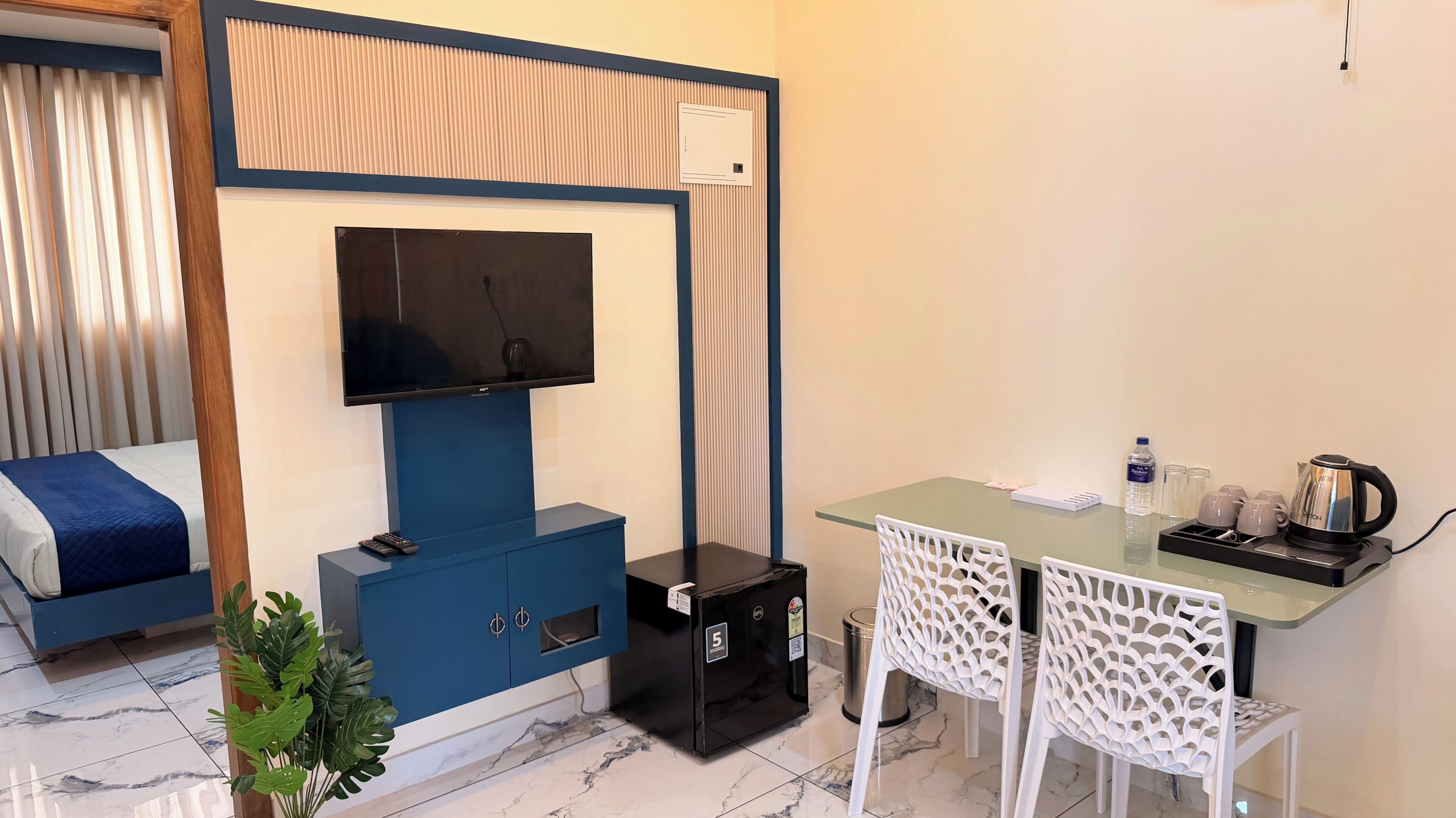 Habitación de hotel con cama, televisión, escritorio con hervidor y cubo de basura.