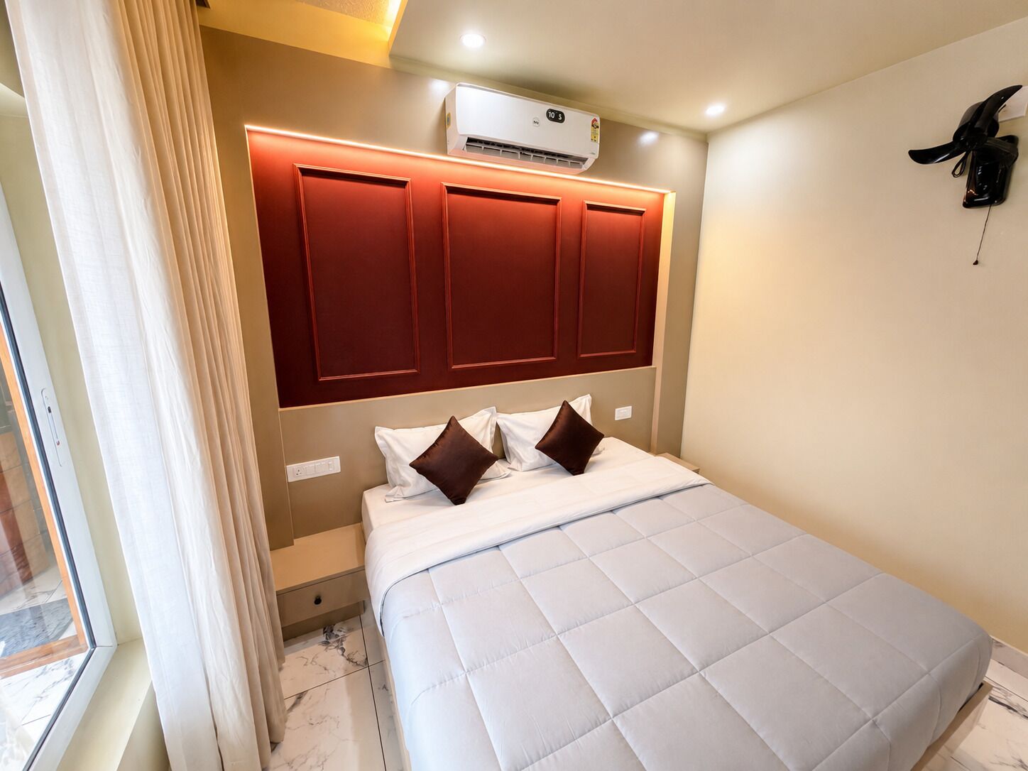 Habitación de hotel con cama, unidad de aire acondicionado, cabecero y ventana con cortinas.