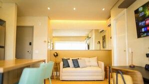 Uma sala de estar moderna com um sofá, uma mesa de jantar e uma TV fixada na parede.