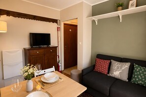 A living room with a TV, sofa, and a dining area with a table set for two. - Via Medal: 1BR apt in the heart of Bardonecchia (Bardonecchia)