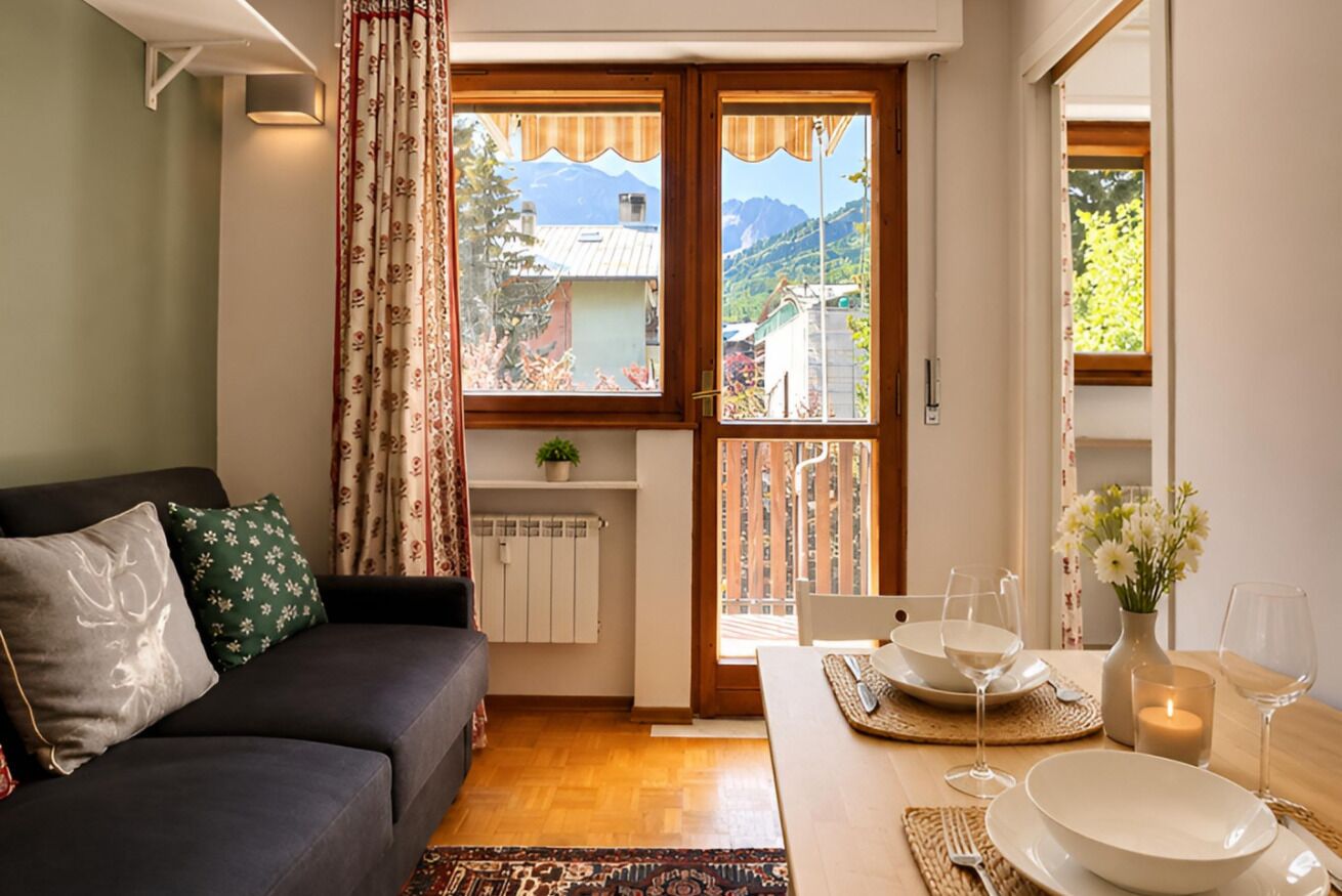 A living room with a sofa, a dining table set for two, and a view of a mountain through a window.