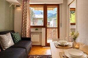 A living room with a sofa, a dining table set for two, and a view of a mountain through a window. - Via Medal: 1BR apt in the heart of Bardonecchia (Bardonecchia)