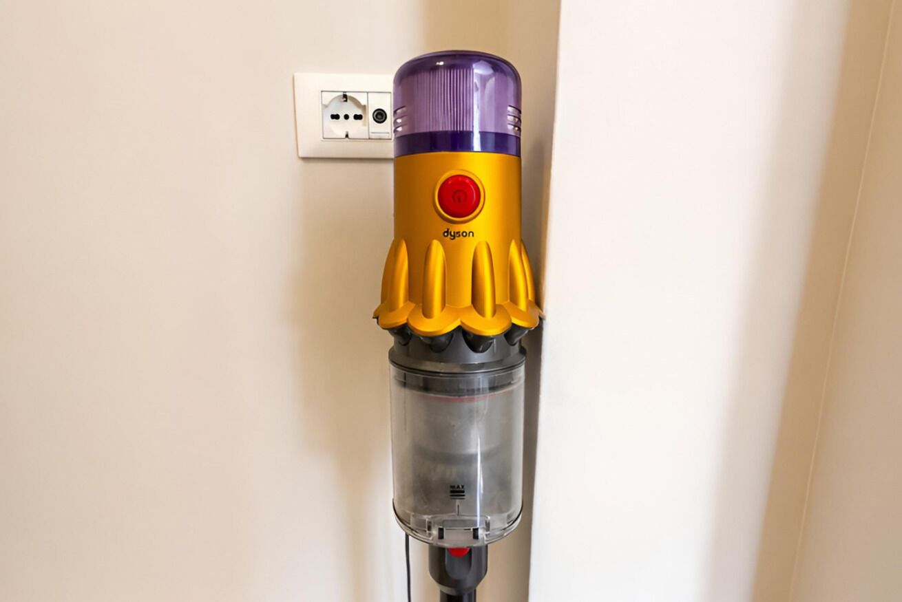 Aspirador Dyson fixado na parede perto de uma tomada elétrica.