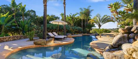 A swimming pool with lounge chairs, surrounded by rocks and tropical plants.
