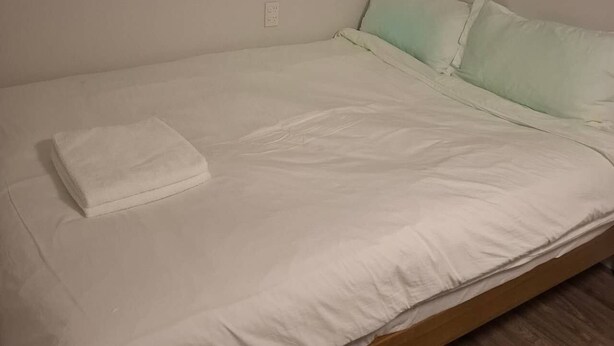 Una cama individual con colchón y almohadas blancas, una toalla blanca doblada y un cabecero de madera.