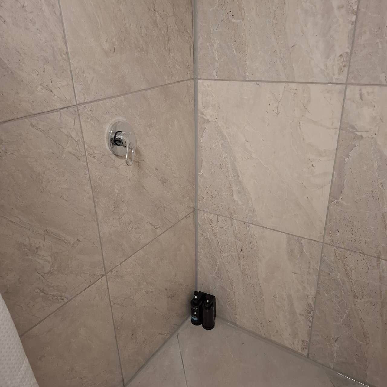 A corner of a room with beige tiled walls and a corner drain.