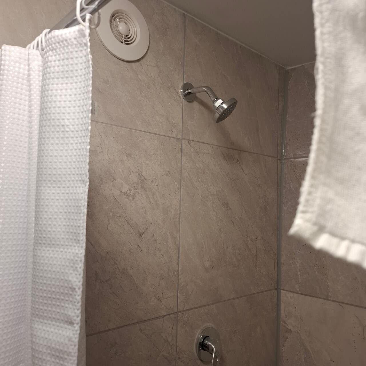 A bathroom with a shower, tiled walls, and a towel hanging on the wall.