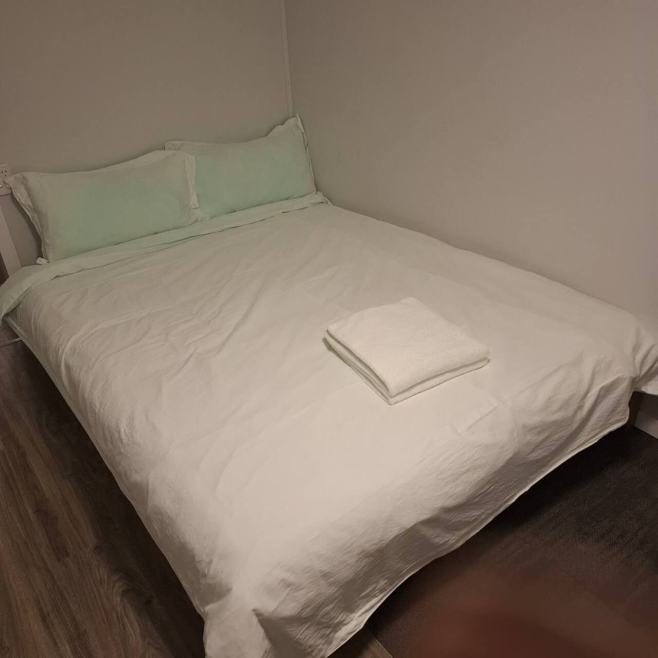 A neatly made bed with a white sheet and a folded white towel on top.