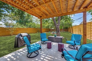 Eine überdachte Terrasse mit Gartenmöbeln, einem Grill und einem Baum.