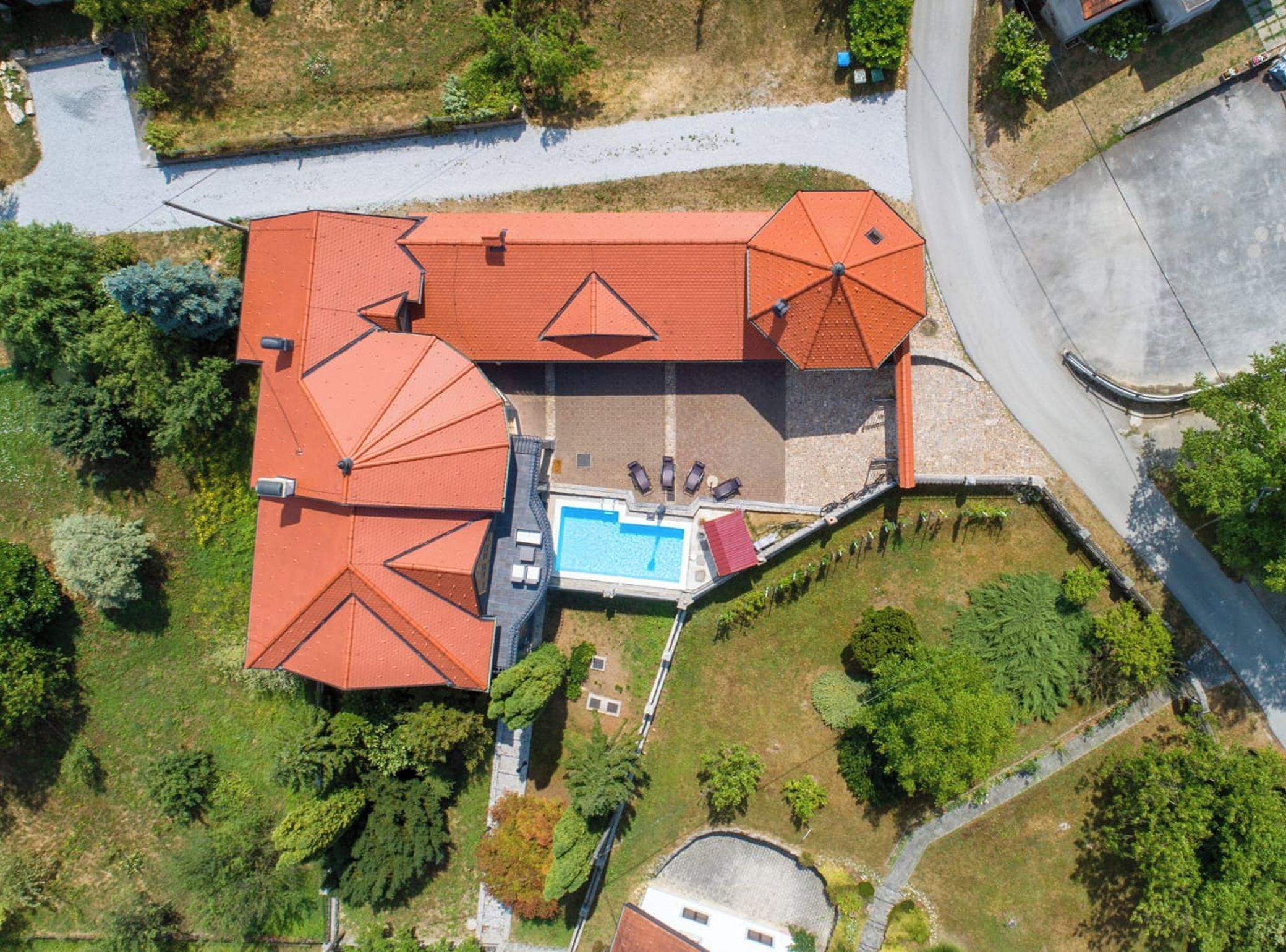 A large building with multiple red-roofed sections, a swimming pool, and surrounding greenery.