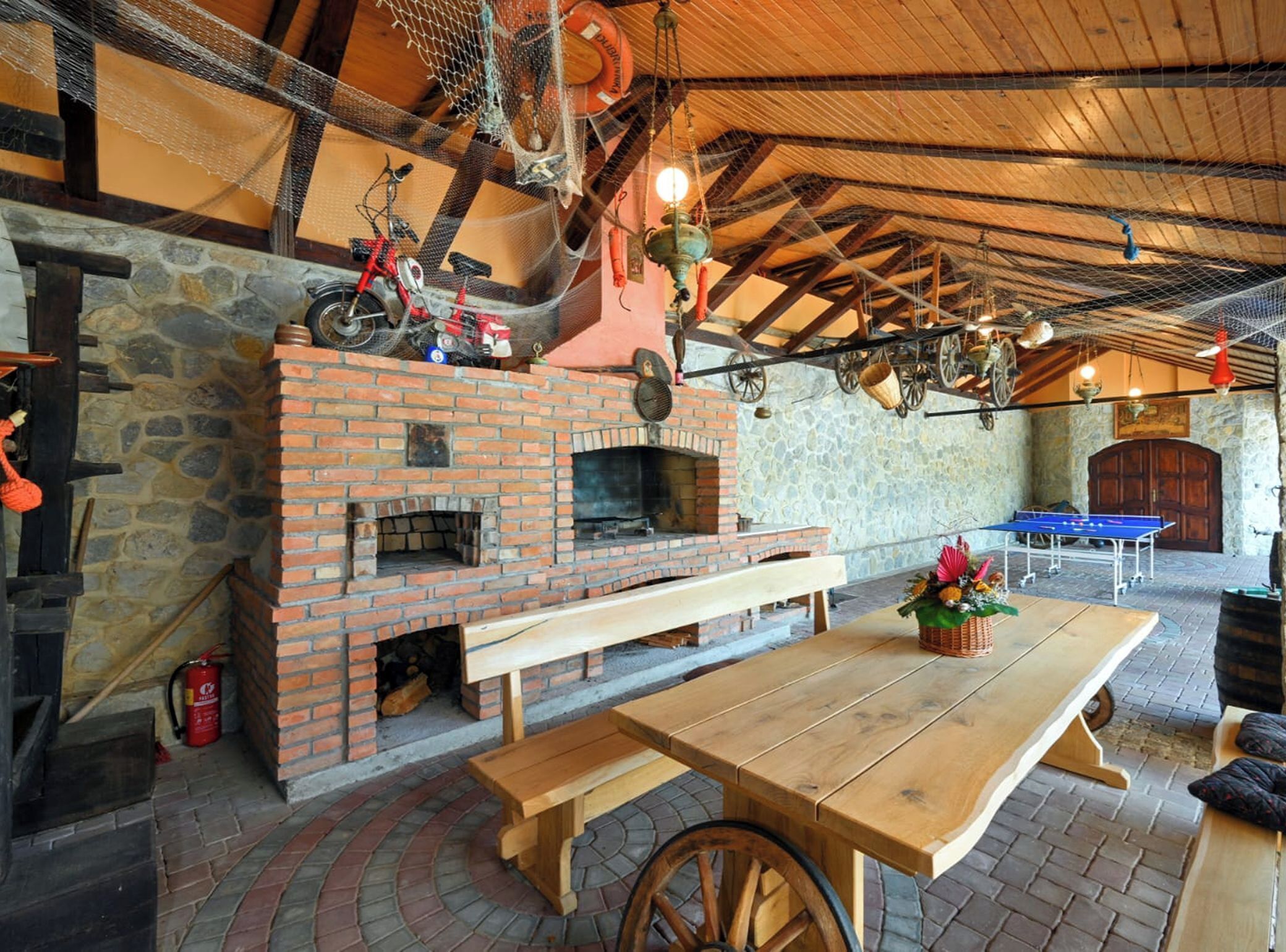 A rustic outdoor dining area with a brick fireplace, wooden benches, and a stone wall.