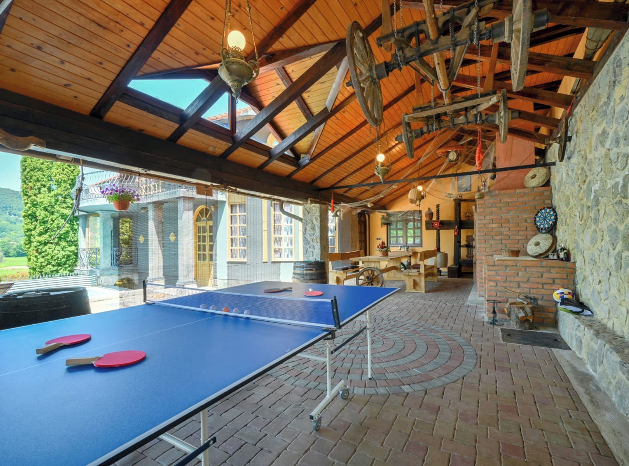 Un tavolo da ping pong all'interno, con pavimento in mattoni, travi in legno e un muro in pietra con bersagli per freccette.