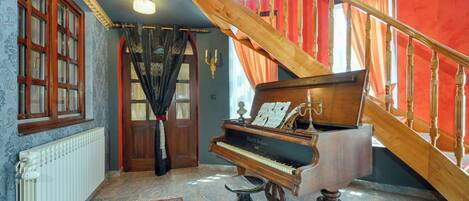 A grand piano in a room with a red staircase, a patterned rug, and a large window with curtains.