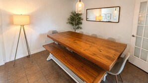 A dining area with a wooden table, benches, chairs, a floor lamp, a potted plant, and a mirror on the wall.