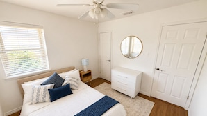 A bedroom with a bed, a nightstand, a dresser, a mirror, and a door.
