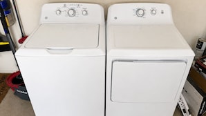 A pair of white front-loading washers with control panels, a mop, and cleaning supplies.