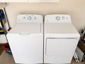 Deux machines à laver à chargement frontal de couleur blanche, dotées de panneaux de commande, un balai-mop et des produits de nettoyage.