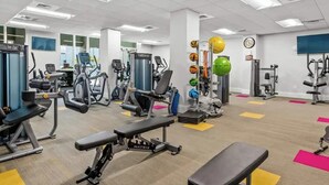 Un gimnasio con diversos equipos de ejercicio, bancos y un estante para pelotas en la pared.