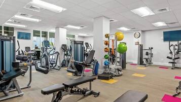 A gym with various exercise equipment, benches, and a wall-mounted ball rack.