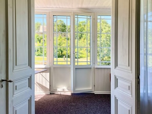 A room with a view of a green landscape through a set of white-framed glass doors. - 8 Person Holiday Home in Kristdala (Kristdala)