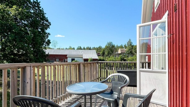 A wooden deck with a round table and four chairs, a red building with windows, and a clear sky. - 8 Person Holiday Home in Kristdala (Kristdala)