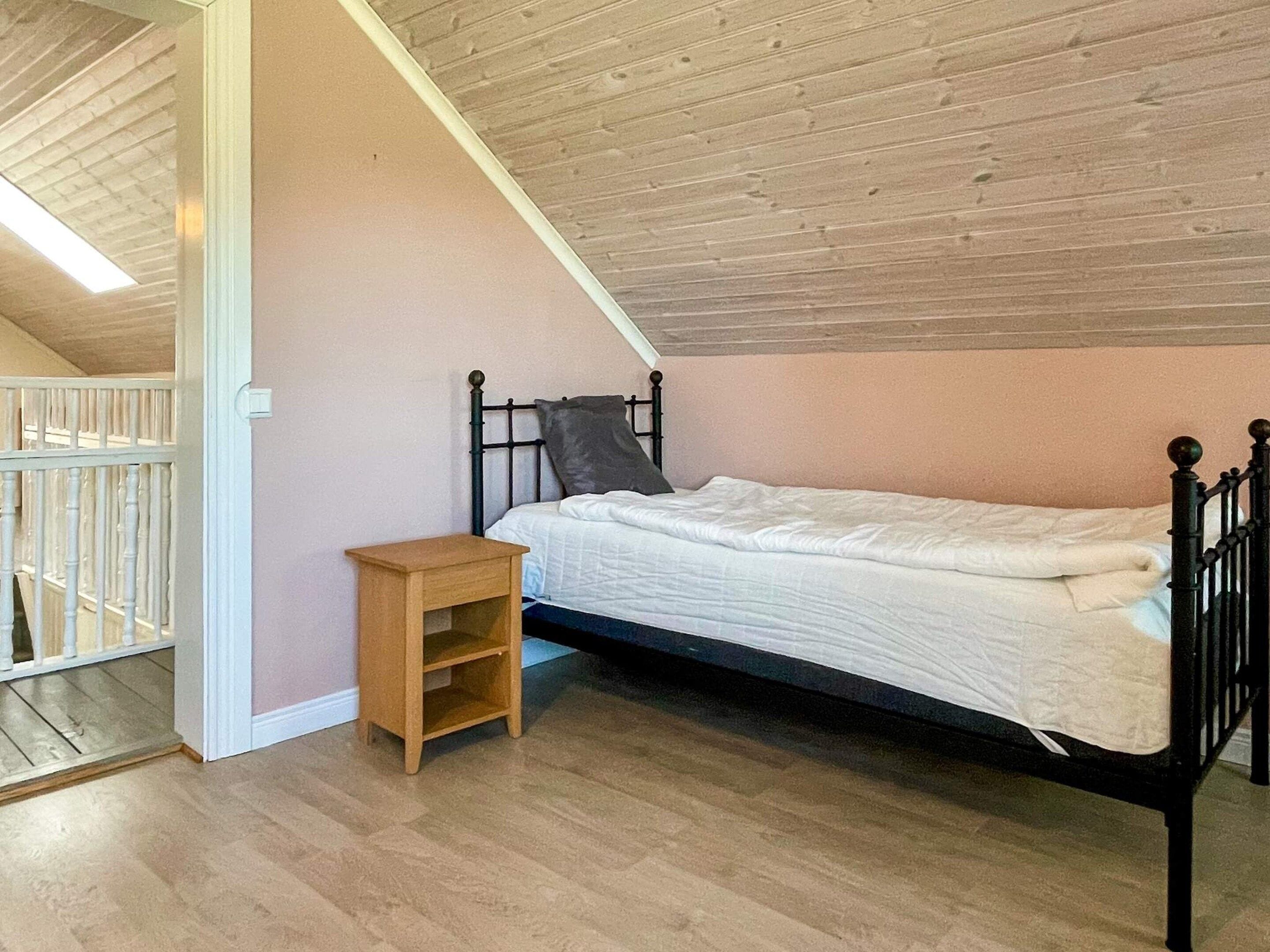 A bedroom with a single bed, a small wooden nightstand, and a white railing.