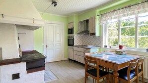 A kitchen with a dining table and chairs, a stove, cabinets, and a window with a view of greenery. - 8 Person Holiday Home in Kristdala (Kristdala)