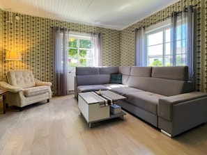 A living room with a sofa, armchair, and coffee table, with patterned wallpaper and large windows. - 8 Person Holiday Home in Kristdala (Kristdala)