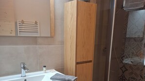 Une salle de bain avec un meuble-lavabo en bois, un évier, une serviette et un espace douche.