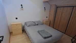Une chambre à coucher comprenant un lit, deux tables de chevet, une armoire en bois et un puits de lumière.