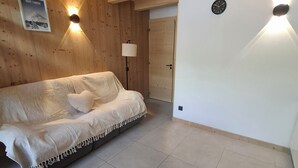 Une pièce avec un lit, des murs en bois, une horloge et une affiche.