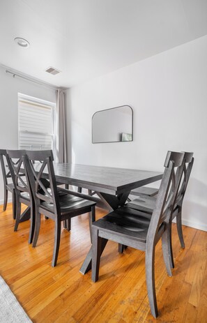 A dining area with a rectangular table, four chairs, a wall-mounted mirror, and a window with curtains. - Cozy 3-bedroom apartment in fantastic Jersey City, easy access to NYC (Jersey City)