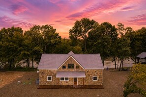A stone building with a gabled roof, surrounded by trees and a body of water. - Waterfront: Hot tub, pool table, river, fishing (McCurtain County)