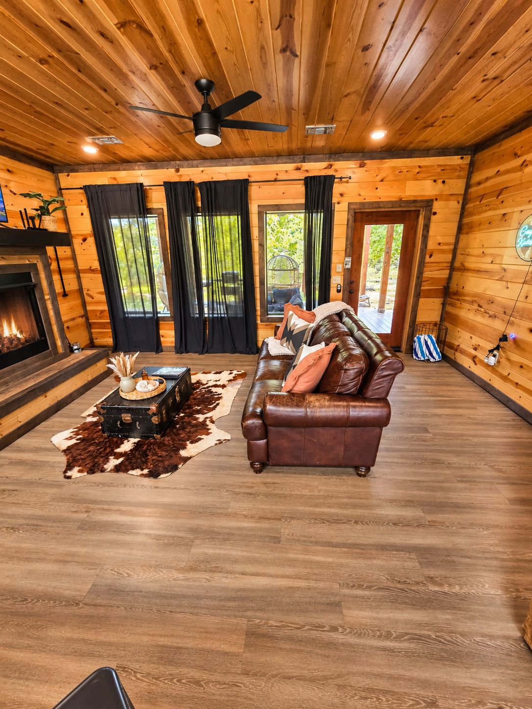 A log cabin interior with a fireplace, leather sofa, and a ceiling fan.