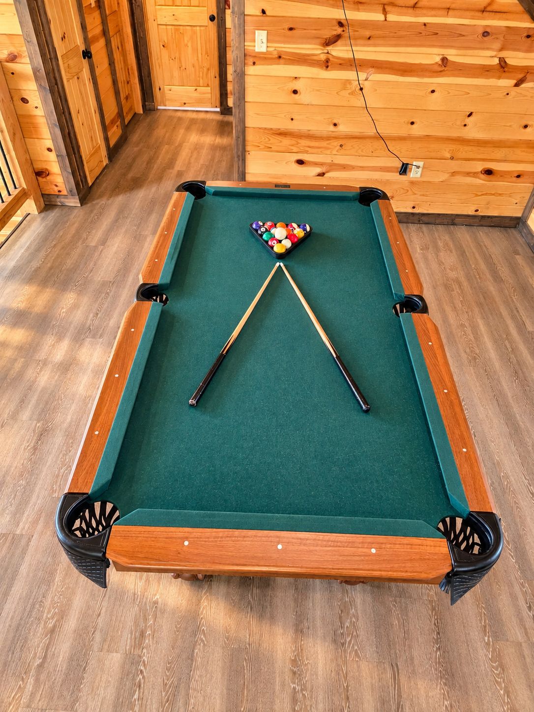 A pool table with a green felt surface, surrounded by wooden walls and floors.