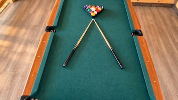 A pool table with a green felt surface, surrounded by wooden walls and floors.