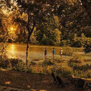 A riverside scene with three individuals standing by the water, surrounded by trees and vegetation. - Waterfront: Hot tub, pool table, river, fishing (McCurtain County)