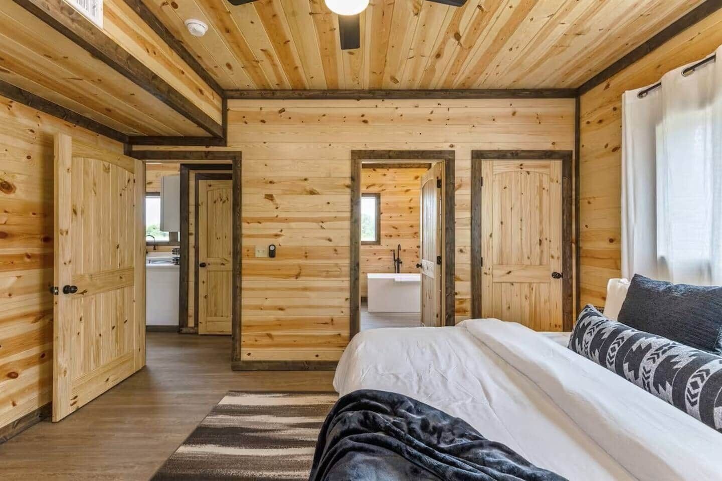 A wooden cabin interior with a bed, a bathroom, and a kitchen area.