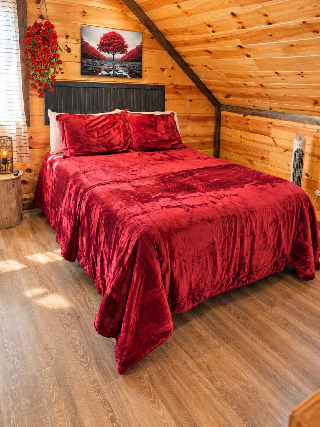 Een slaapkamer in een houten blokhut met een rode sprei, een schilderij van een boom en een bloemstuk.