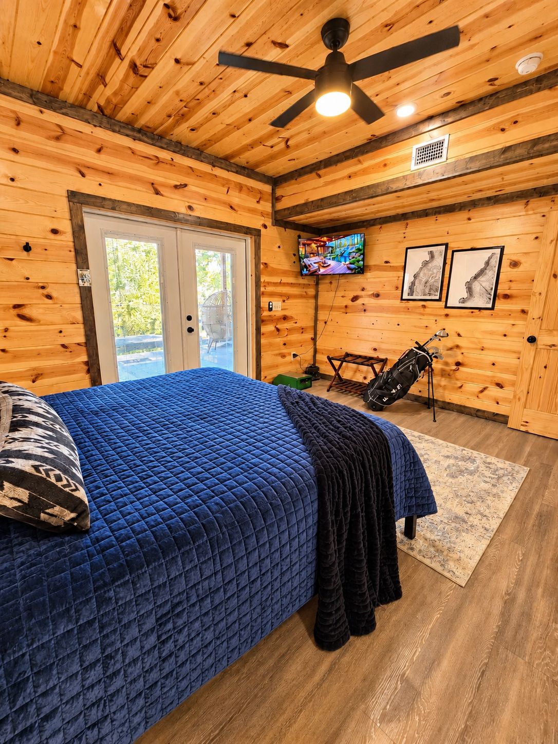 A bedroom with a bed, a ceiling fan, a television, and a door leading outside.