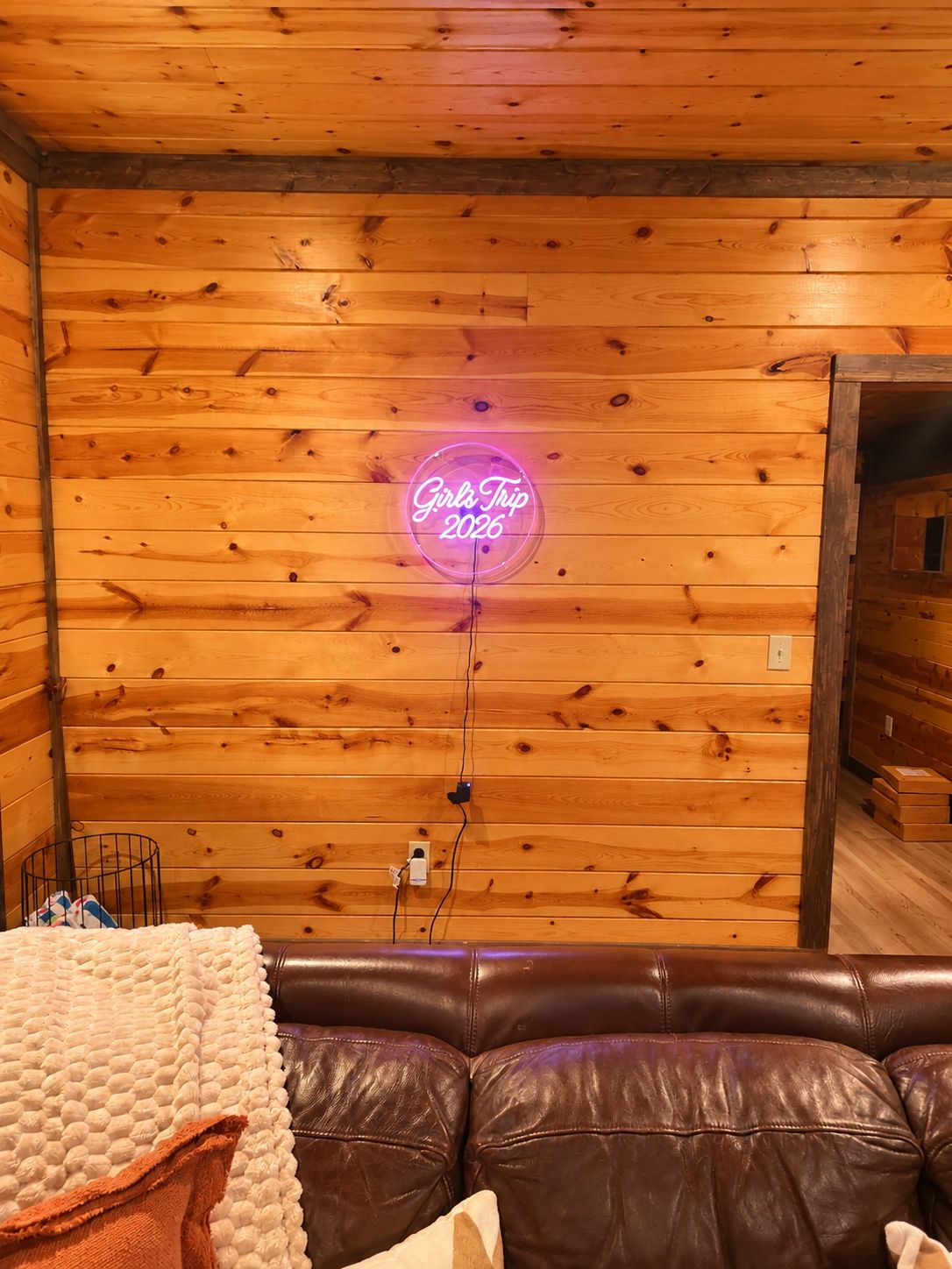 Un interno accogliente di una baita, con un cartello luminoso al neon, un divano in pelle e rivestimenti in legno.