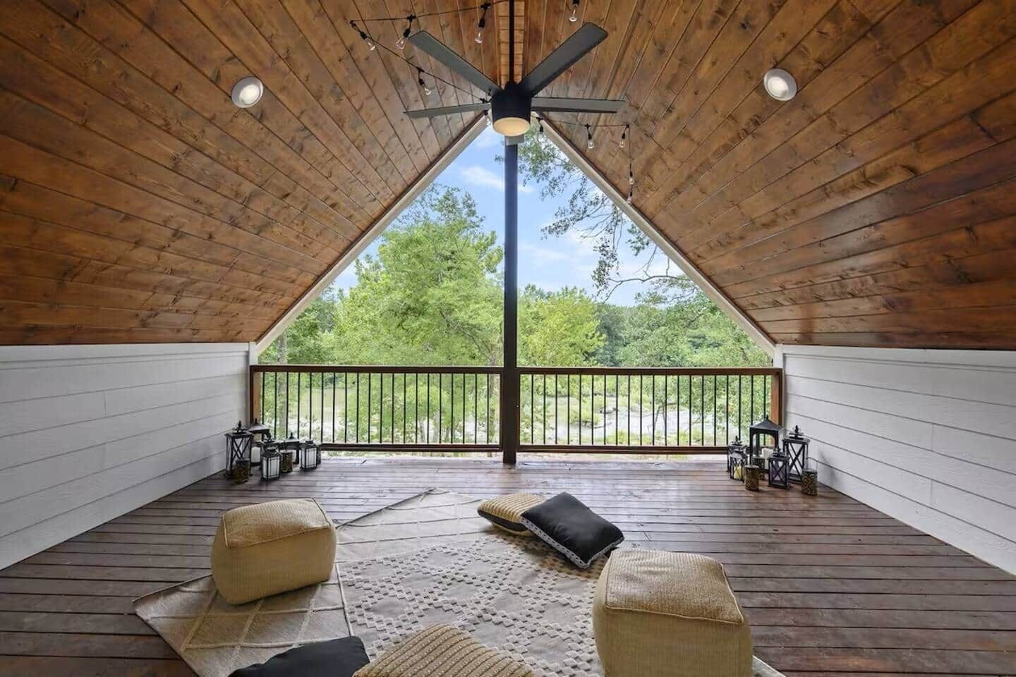 A spacious attic room with a sloped ceiling, a large window, and a balcony with outdoor furniture.