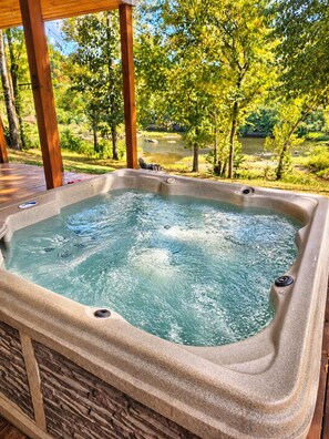 Een hottub met een stenen buitenkant, omgeven door een houten terras en bomen, met uitzicht op een natuurlandschap.