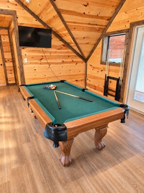A pool table in a wooden room with a sloped ceiling and a television mounted on the wall. - Waterfront: Hot tub, pool table, river, fishing (McCurtain County)