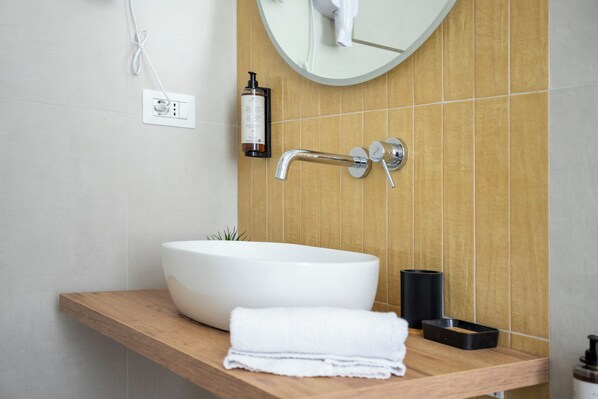 A modern bathroom with a large white sink, a mirror, a towel, and a bottle of shampoo. - Trastevere suites guest house (Rome)