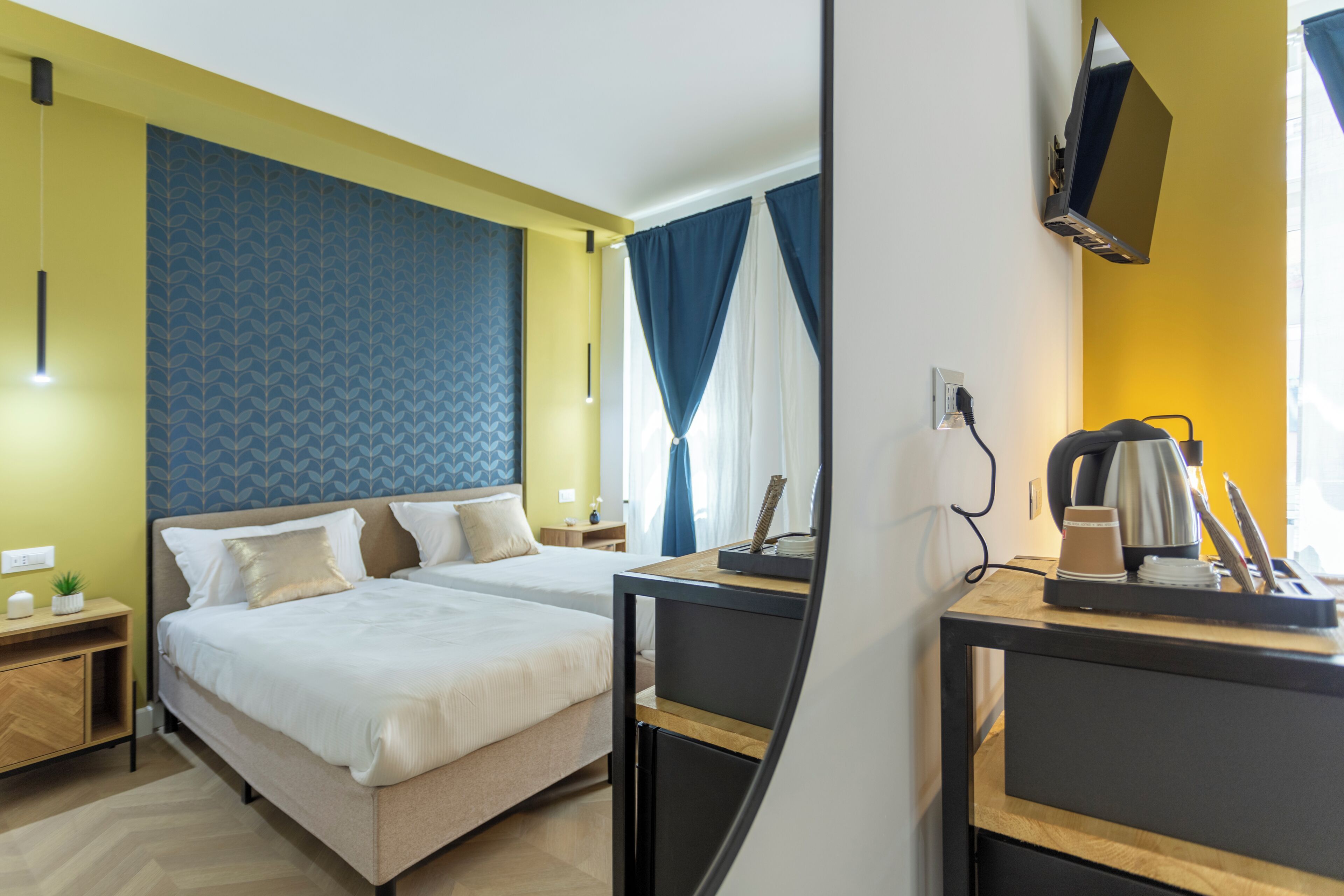 A hotel room with two beds, a desk with a coffee maker, a TV, and a nightstand with a lamp.