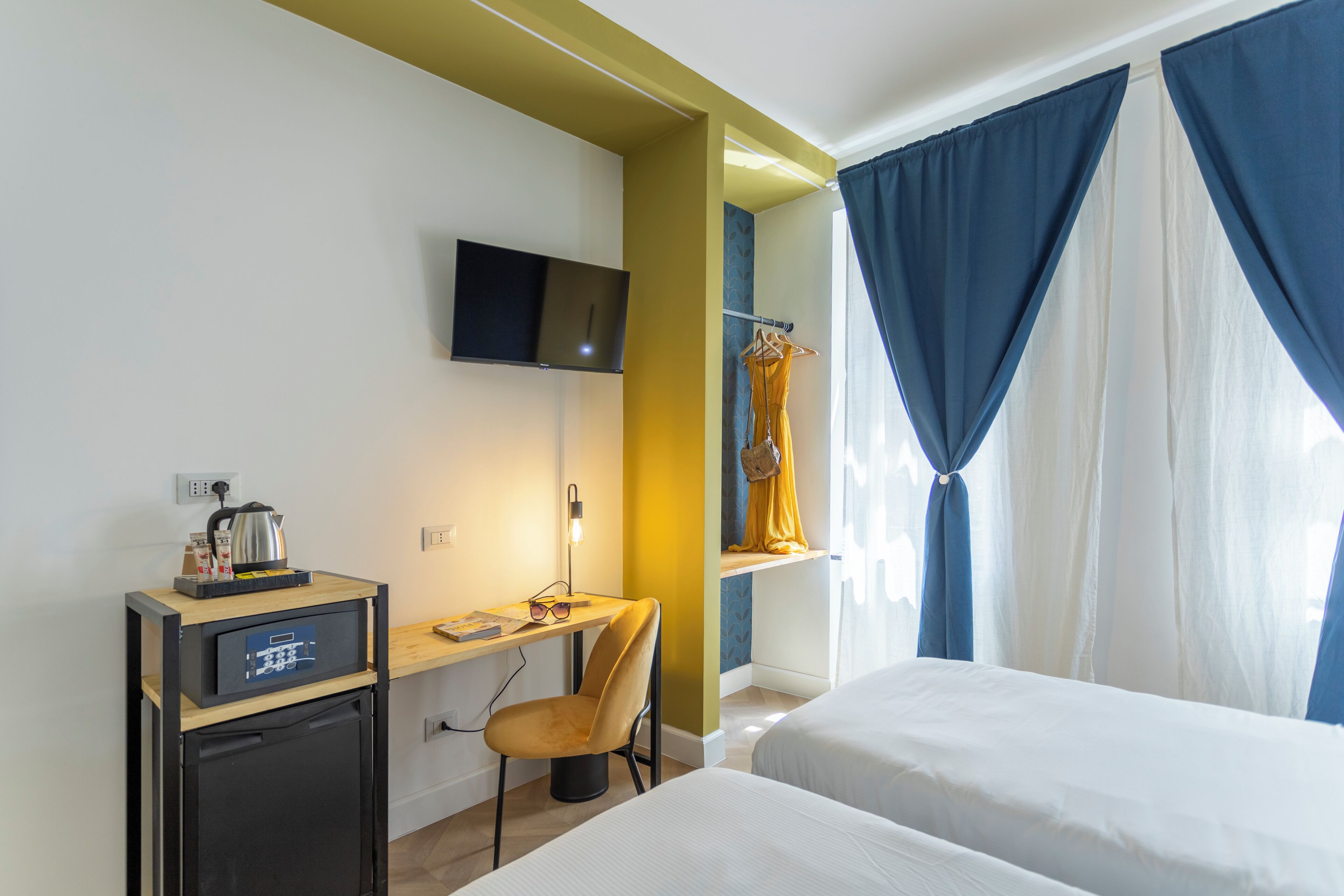 A hotel room with a bed, a desk with a television, a chair, and a wardrobe.