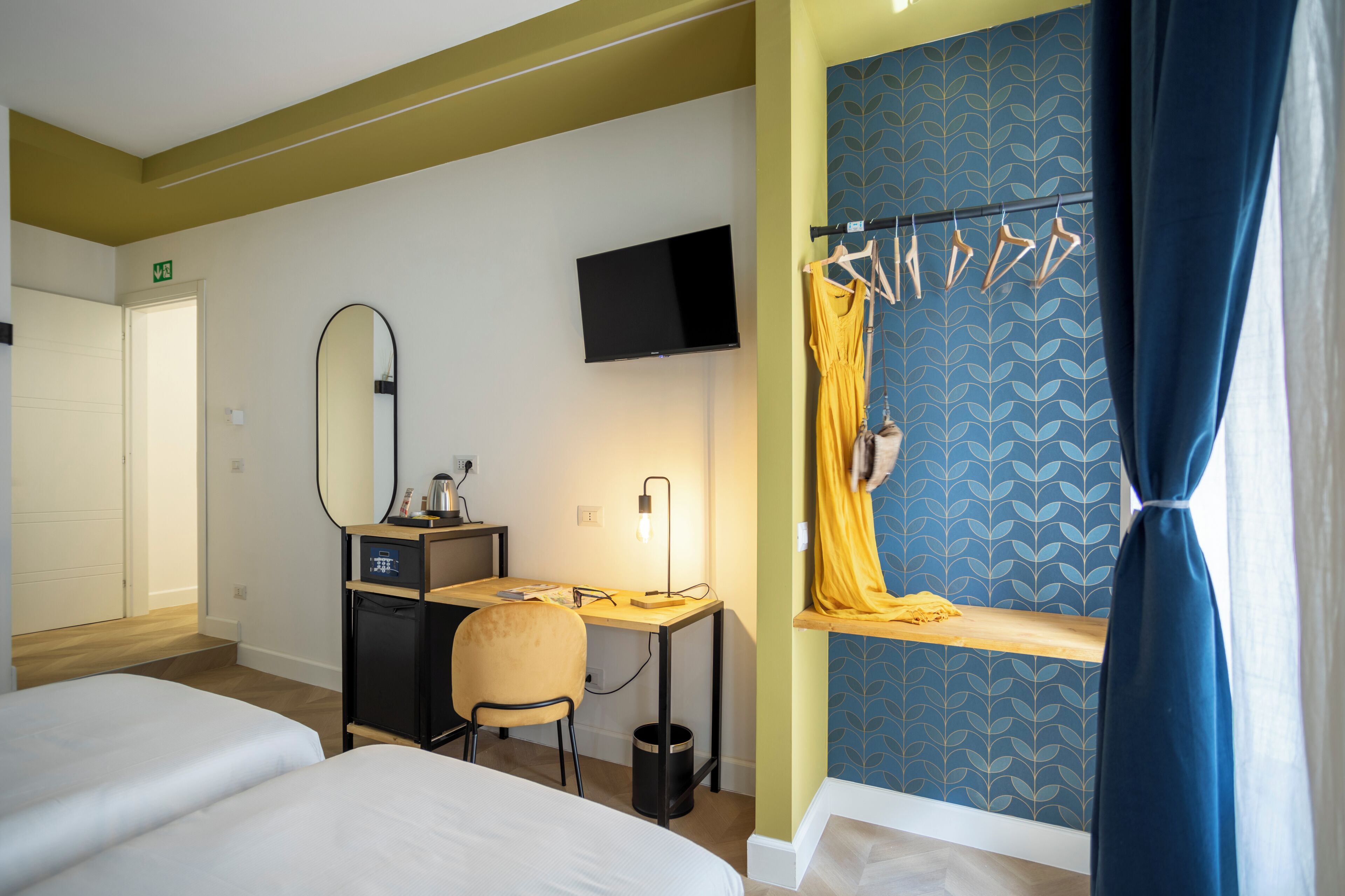 A hotel room with a desk, chair, bed, TV, and a window with curtains.