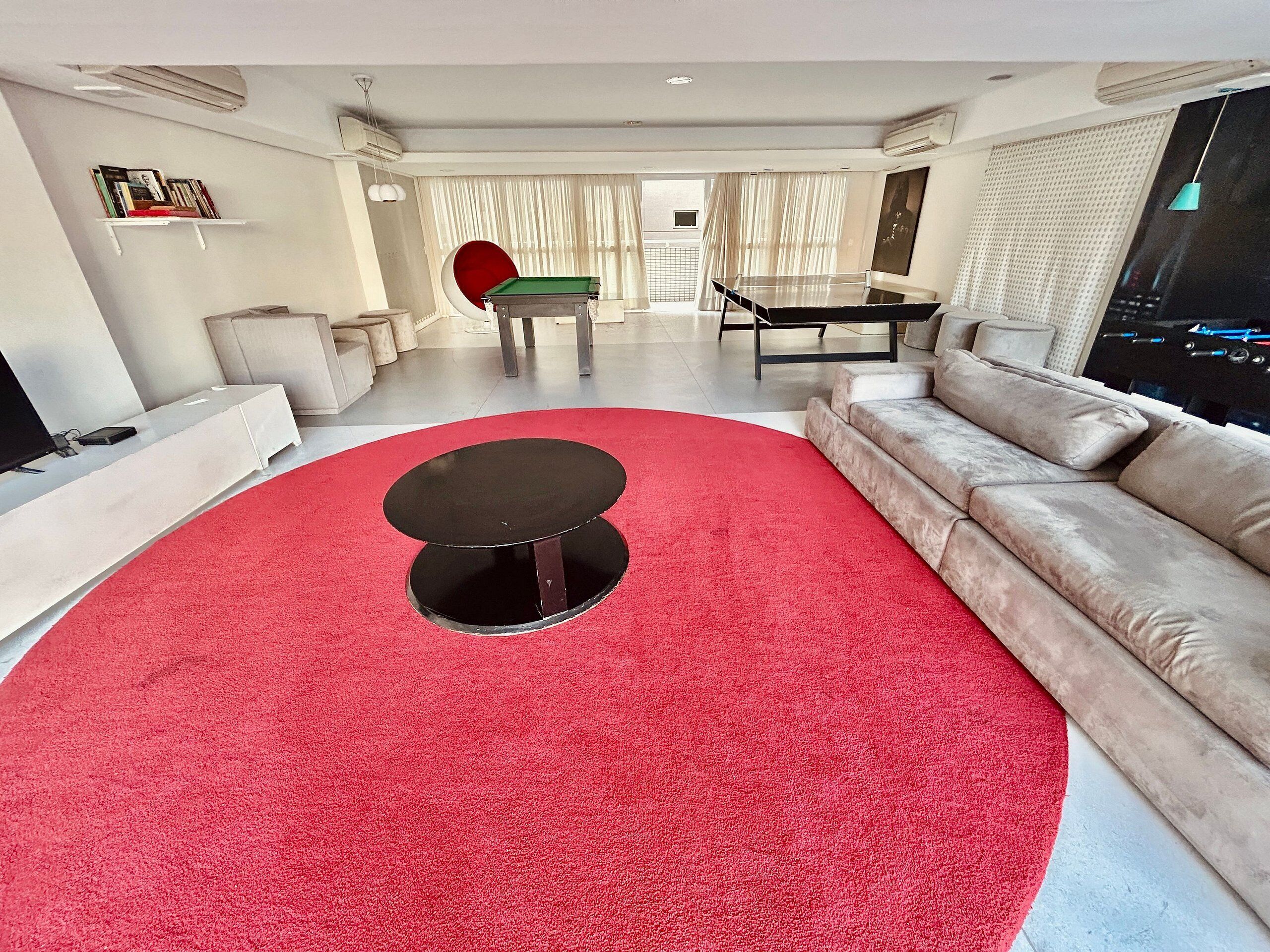Una sala de estar moderna con alfombra roja, una mesa de centro redonda negra, un sofá beige, una mesa de comedor y un televisor.